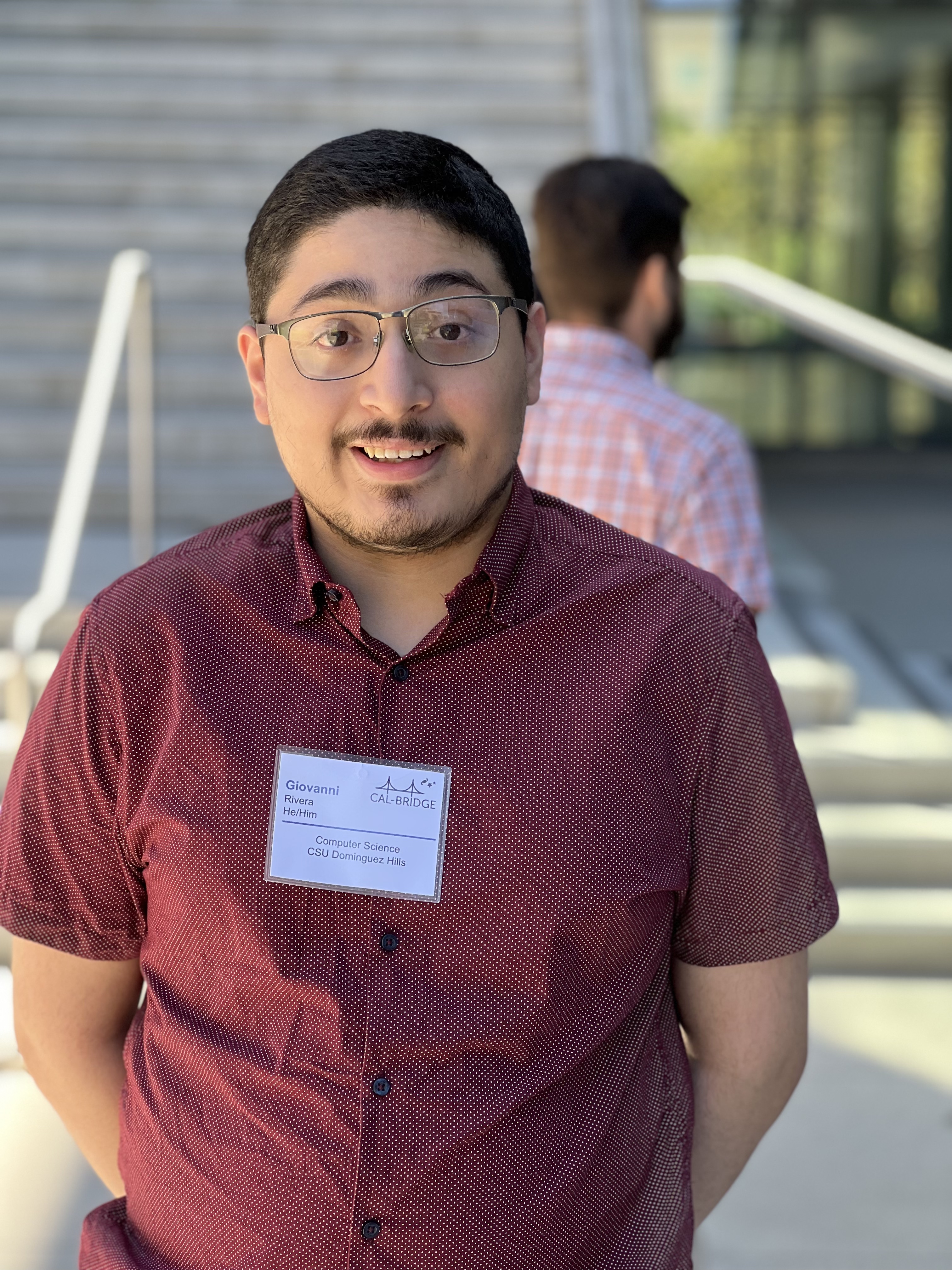 Giovanni in a red shirt with a name tag from the Cal-Bridge program.