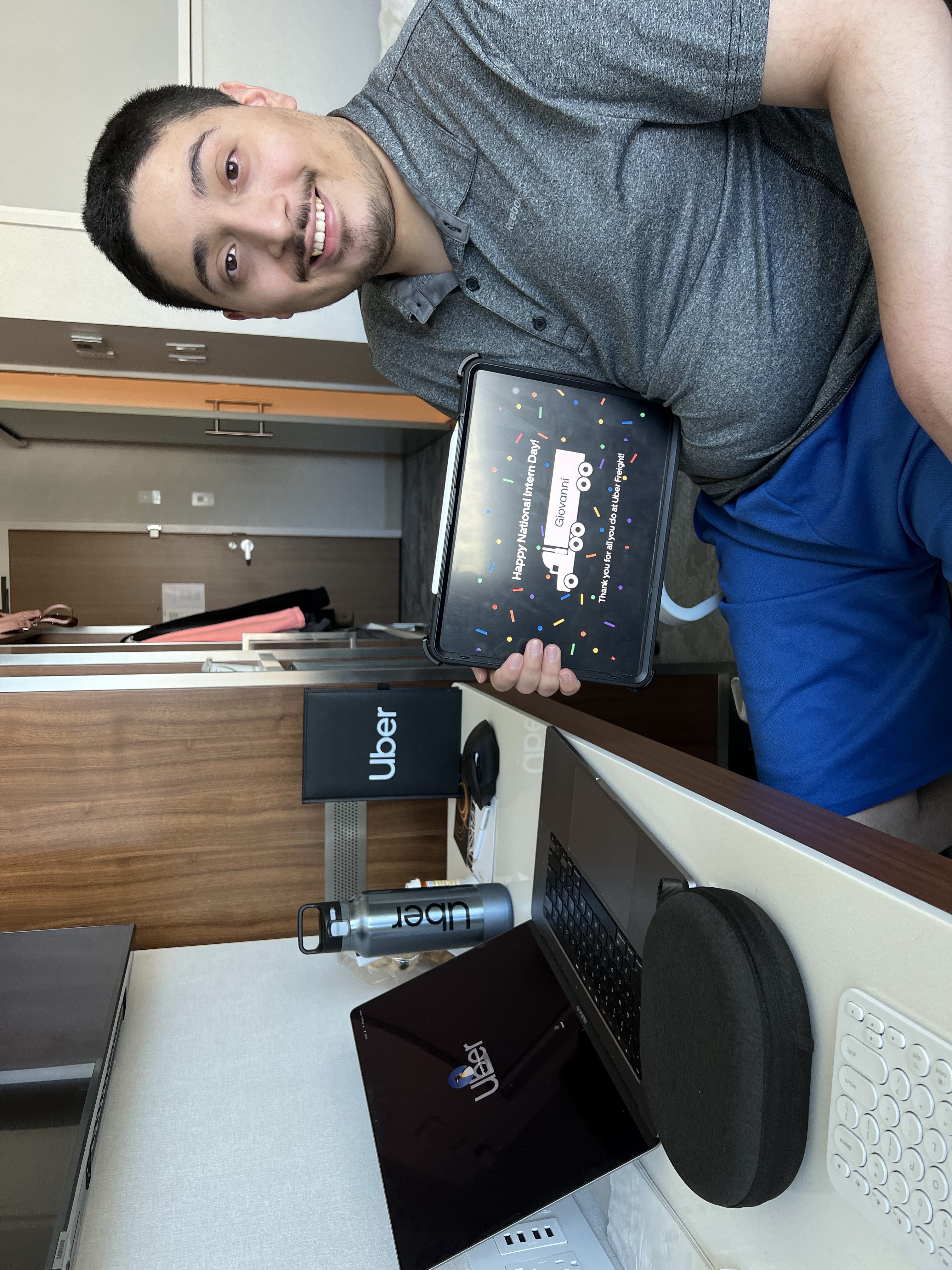 Giovanni holding a digital intern day card with a MacBook, Water Bottle, and Bottle with the Uber brand.